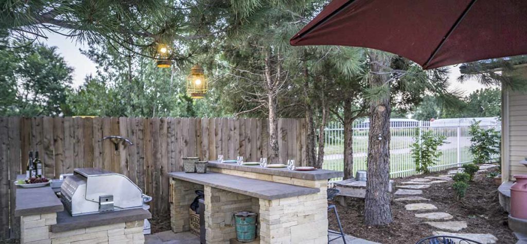 This outdoor kitchen is lit up with two standard 120v light fixtures hanging from the pine trees.